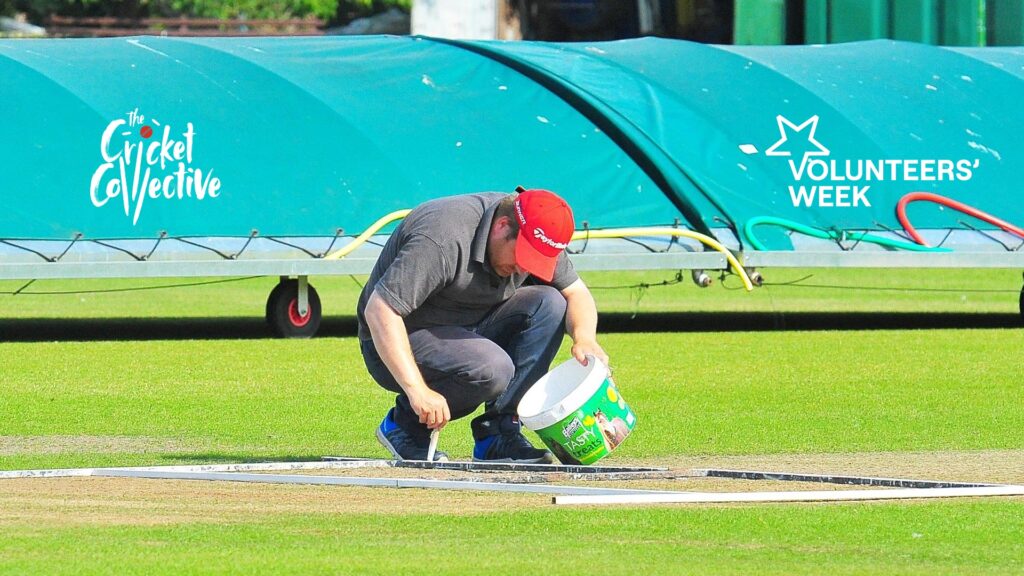 Grounds person kneeling down on cricket square applying white paint to mark out batting crease.