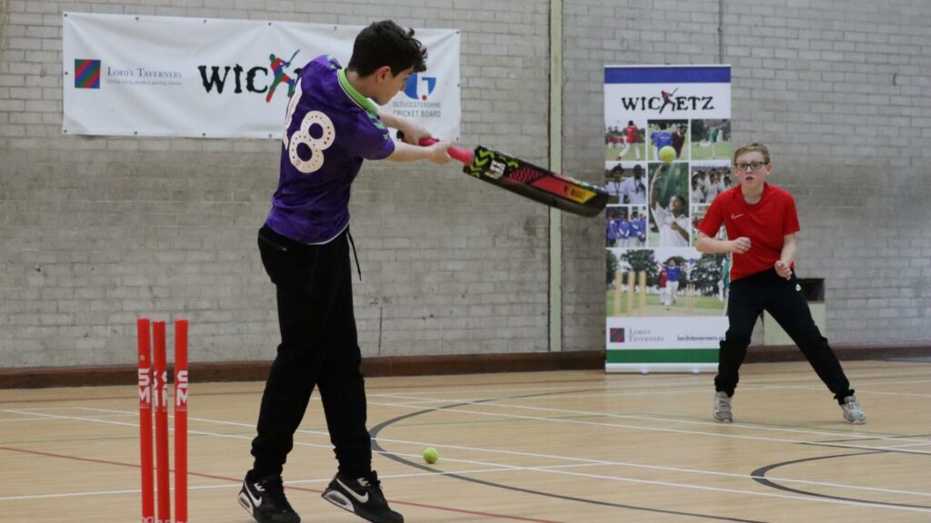 Two young people playing cricket in a hall